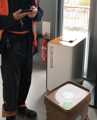 Poubelle pour le tri de déchets organiques en entreprise Une poubelle métallique avec l'inscription "biodéchets" sur la porte. Un collecteur de OuiCompost à côté de la poubelle est en train de réaliser la collecte de biodéchets à Lyon et rentrer les données de la collecte dans la base de données OuiCompost.