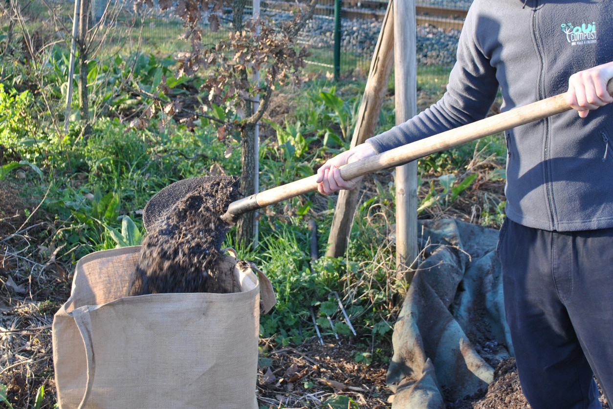 Acheter du compost à Lyon en vrac Un agent de OuiCompost remplit un grand sac en jute avec du compost à la pelle.